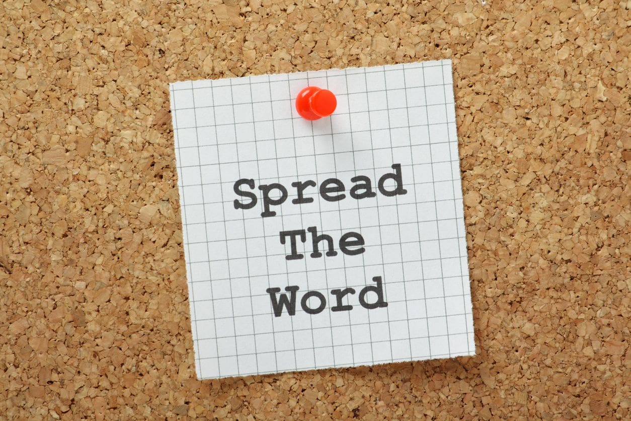 A note pinned to a cork board with the words spread the word.