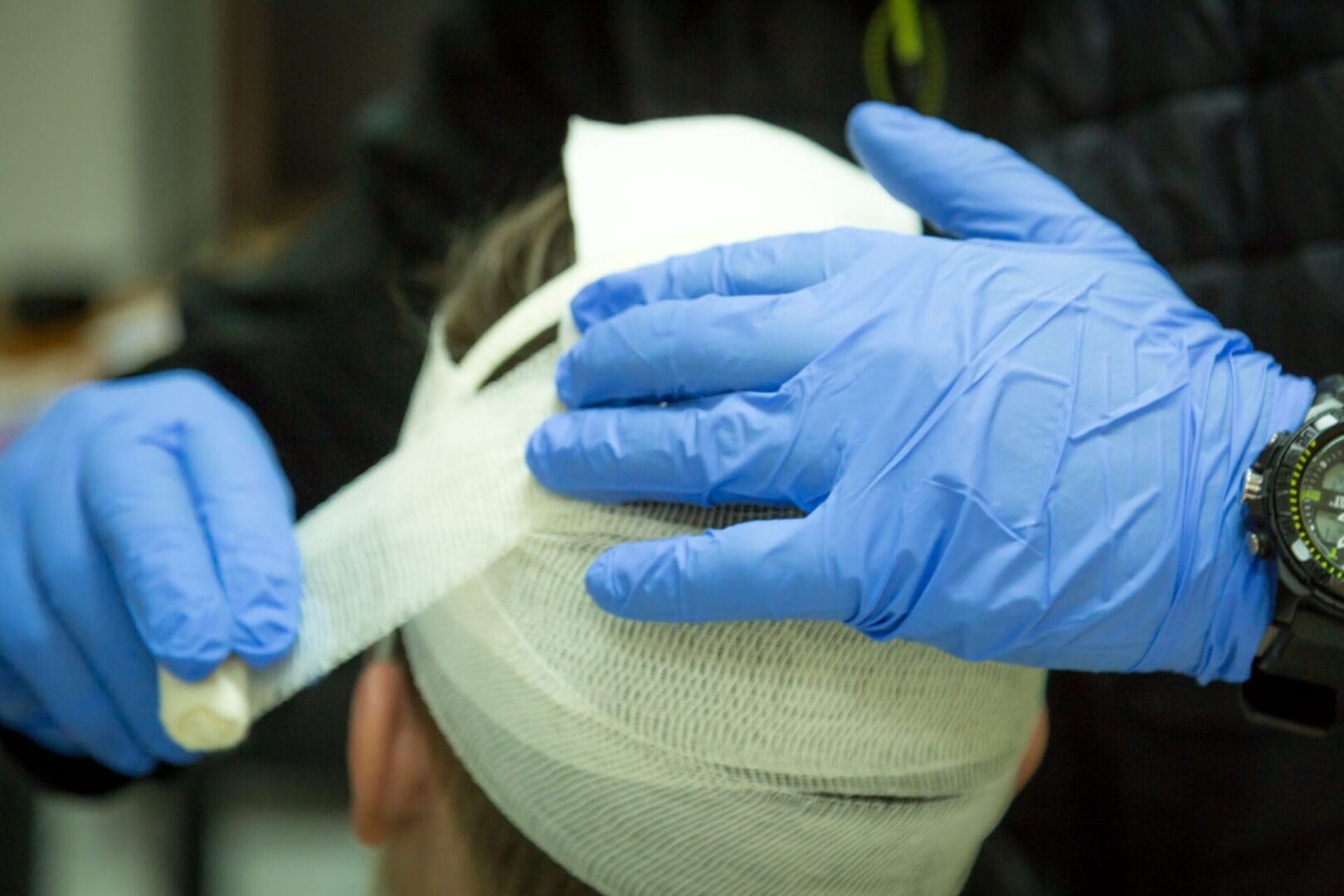 A person with blue gloves is bandaging their head.